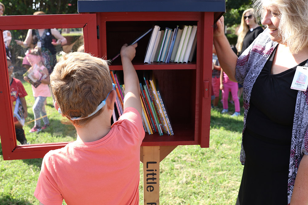 a young boy places books inside a little free library