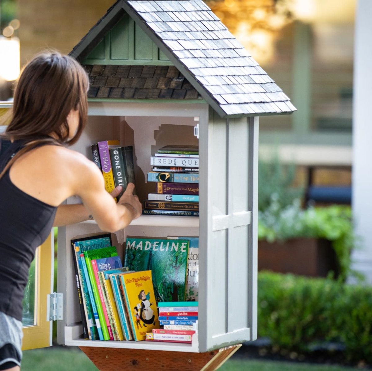 a young woman places books inside a little free library