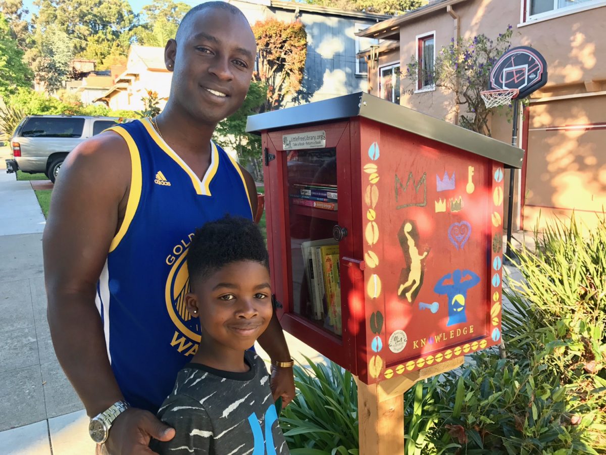 young male adult and young male child standing next to a decorated little free library